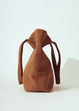 Bolso tipo tote bag de gamuza color marrón, con asas trenzadas y paneles laterales con detalle de trenzado vertical.