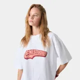 Remera blanca de corte holgado con estampado frontal con la palabra 'MESTUDIOS' en color rosa y rojo.