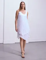 Vestido blanco de gasa con escote redondo bordado con apliques metálicos. Tiene forro interno a tono y ruedo en capas asimétricas.