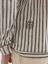 Chomba a rayas horizontales color crudo y gris, con capucha y botones de madera. Tiene cordones de ajuste en la capucha y puños con ribete verde flúor.