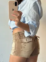 Short de jean color marrón claro con efecto desgastado, tiro alto, cierre con cordones cruzados y detalles rotos.
