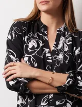 Blusa de gasa estampada con flores blancas sobre fondo negro, marca Floral & Ivy. Tiene cuello a la base con escote en V y mangas tres cuartos regulables con presilla y botón.