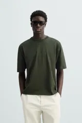 Camiseta verde oscuro de corte holgado, confeccionada en tejido de algodón grueso. Tiene cuello redondo y mangas cortas sin costura en la sisa.