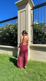 Vestido largo de microtul color rojo, con escote profundo en V y cuello halter. La falda presenta un diseño con frunces, transparencias y un tajo lateral pronunciado con detalle de volados.