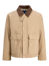 Chaqueta estilo workwear color arena con cuello marrón de pana y acabado satinado. Tiene cierre frontal con botones a presión, mangas largas, bolsillos frontales tipo parche y puños abotonados.
