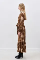 Vestido largo de viscosa estampada en tonos marrón y beige, con escote en V, mangas largas con puños elásticos y volado en el ruedo. Incluye lazo del mismo género para ajustar en la cintura.