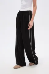 Pantalón deportivo negro de corte ancho y tiro alto, con cintura elástica y cordón ajustable. Presenta una raya blanca vertical a cada lado.