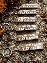 Llavero 3D de plástico PLA color beige con la frase "Refuse to Lose" en letras blancas.
