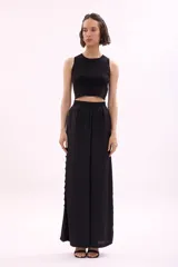 Pantalón de tela color rosa pálido, de corte palazzo y cintura alta con elástico. Presenta aberturas circulares verticales en los laterales.