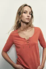 Remera blanca de manga corta con escote redondo y cordones cruzados con ojalillos metálicos.