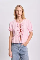 Blusa rosa con rayas verticales blancas, escote redondo con lazos decorativos, mangas cortas abullonadas y corte peplum.
