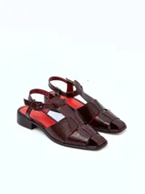 Sandalias de cuero color borgoña con textura croco, diseño cerrado en la parte delantera con aberturas laterales, punta cuadrada y cierre con hebilla ajustable en el tobillo. Taco ancho de 3 cm.
