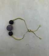 Pulsera dorada con tres piedras volcánicas negras y cierre corredizo.
