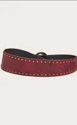 Cinturón ancho de cuero color rojo con diseño floral repujado, tachas doradas y hebilla circular de metal envejecido.