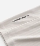 Remera deportiva de manga corta y cuello redondo, color beige claro, con textura acanalada vertical. Presenta detalles reflectantes en los hombros.