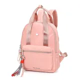 Mochila rosa de tela con doble asa de mano y tiras traseras regulables. Tiene un bolsillo frontal con cierre y un dije colgante con borlas.