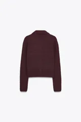 Chaqueta de punto color borgoña, con cuello camisero y manga larga. Tiene falsos bolsillos con solapa en el delantero y cierre frontal con botones metálicos dorados.
