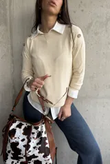 Sweater beige de hilo con cuello camisero blanco y botones decorativos en los hombros.
