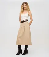 Pollera midi color beige confeccionada en sarga de algodón certificado BCI, con cintura alta y pasadores, bolsillos frontales, recorte en la cadera con frunces y cierre de botón y cremallera.