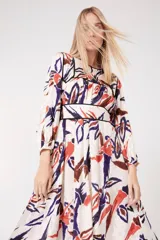 Vestido largo de viscosa con estampado abstracto en tonos naranja, marrón y violeta sobre fondo blanco. Tiene mangas largas abullonadas, cuello redondo y corte a la cintura con ribete negro.