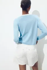 Chaqueta celeste de punto con cuello redondo y manga larga. Tiene cierre frontal con botones y detalle de falsos bolsillos delanteros con ribete blanco.