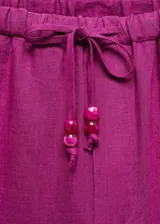 Pantalón crop color fucsia de tejido de lino, tiro medio, cintura elástica con lazo, diseño jogger y bolsillos laterales.