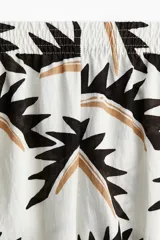 Pantalón de corte holgado con cintura elástica de tiro alto, bolsillos laterales discretos y piernas amplias, con estampado geométrico en tonos negro, marrón y blanco.