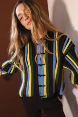 Cárdigan tejido con lurex, con cuello redondo, manga 3/4 y cierre frontal con botones forrados. Diseño con rayas verticales en tonos verde, azul y violeta sobre fondo negro con brillo.