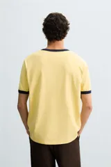 Camiseta amarilla de corte regular fit, cuello redondo y manga corta. Tiene un bordado frontal de texto en color azul marino. Acabados con rib a contraste en cuello y mangas.