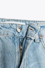 Pantalón de jean de tiro medio con cinco bolsillos, corte wide leg y detalle de tejido con lavado lateral combinado. Cierre frontal con cremallera y botón.