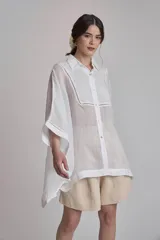 Camisa blanca de lino con cuello clásico, cierre frontal con botones y mangas anchas 3/4. Presenta detalles de bordado calado en el frente y puños.
