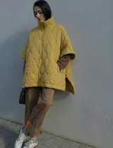 Poncho acolchado color mostaza con cuello alto y abertura frontal con cierre. Presenta un patrón capitoné de formas ovaladas y bolsillos delanteros.