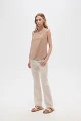 Blusa color beige de poliéster, sin mangas, con cuello asimétrico y detalle de drapeado en los hombros.