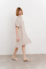 Vestido camisero corto color verde oliva, confeccionado en lino 100%. Tiene botones en la parte delantera, cuello camisero, mangas cortas con botón para arremangar y bolsillos laterales.
