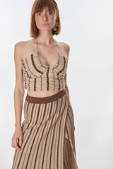 Top corto color beige con rayas verticales marrones, escote halter y espalda descubierta. Tejido de punto con lurex.