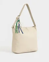 Cartera tipo saca color crudo, de cuerina, con asa corta regulable para el hombro y cierre superior. Incluye charms decorativos colgantes.
