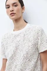 Blusa de manga corta color crudo, con cuello redondo y diseño de encaje bordado floral.