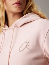 Buzo rosa claro de felpa de algodón con capucha y cordones ajustables. Tiene puños y bajo acanalados, y logo de Calvin Klein bordado en el pecho.