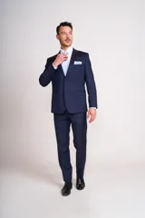 Traje de vestir azul marino, compuesto por saco de dos botones con solapa de muesca, dos bolsillos laterales con solapa y un bolsillo de ojal en el pecho, y pantalón de vestir con corte recto. Incluye camisa blanca, corbata celeste y pañuelo de bolsillo blanco con borde celeste.