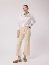 Camisa blanca de algodón con cuello clásico, cierre frontal con botones y mangas largas. Presenta bordados calados con motivos florales en la parte superior.