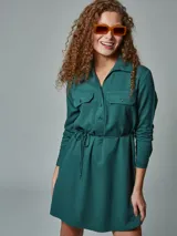 Vestido camisero verde con cuello clásico, mangas largas, cierre frontal con botones, dos bolsillos con solapa en el pecho y cinturón con lazo.