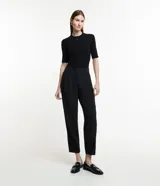 Pantalón negro de corte carrot, con pliegues delanteros, abotonado frontal y detalle en el bajo.