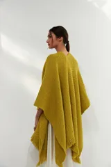 Ruana tejida color verde pistacho con flecos en el borde inferior y parche de cuero en la parte inferior.