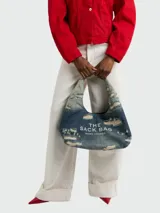 Bolso de hombro Marc Jacobs modelo The Sack Bag, confeccionado en denim azul con efecto desgastado y roturas. Presenta el logo de la marca estampado en el frente.