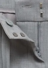Pantalón gris de tiro medio y corte ancho, con bolsillos laterales, cierre oculto con botón, gancho y cremallera, y forro interior.