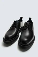 Zapato de vestir estilo derby, color negro, con capellada de cuero, horma redonda y suela de goma con volumen.