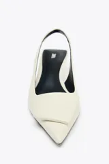 Zapato destalonado color crema con tacón fino y adorno en la parte delantera.