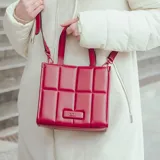 Cartera tote chica color bordó, confeccionada en símil cuero con diseño acolchado y logotipo metálico de XL Extra Large al frente. Tiene acceso con cierre, correa regulable, un bolsillo interno con cierre y otro abierto.