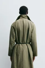 Trench color verde oliva de tejido técnico, corte relaxed fit, cuello solapa, manga larga, bolsillos laterales y abertura en la espalda.