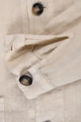 Campera color crema estilo sobre camisa hecha en lino premium con cuello clásico, cierre con botones marrones, dos bolsillos de parche inferiores y un bolsillo de parche superior.